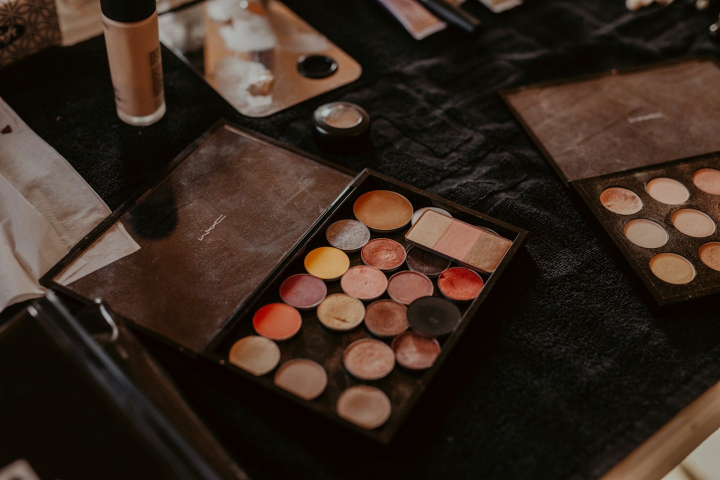Palette di trucchi, fondotinta e tavolozza di miscelazione su tessuto scuro.