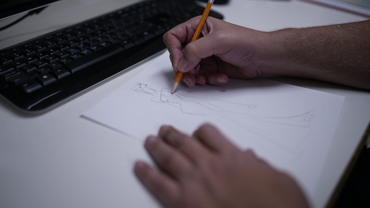 Mani usano una matita gialla per disegnare un abito.